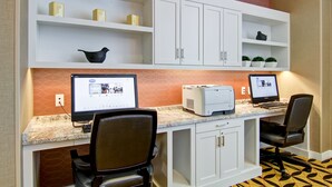 Un espacio de trabajo con dos escritorios, cada uno con una computadora e impresora. Hay armarios blancos sobre los escritorios y un piso con diseño.