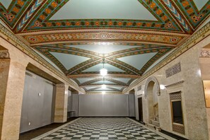 Un pasillo con piso a cuadros, techo ornamentado con diseños geométricos y una araña.