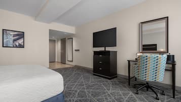 A hotel room with a bed, a flat-screen TV, a desk with a chair, and a patterned carpet.