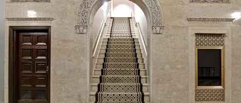 Una escalera de mármol con diseños intrincados, flanqueada por puertas ornamentadas y un suelo con motivos.