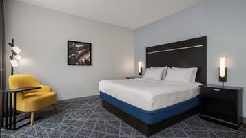 A hotel room with a bed, a chair, a nightstand, and a wall-mounted picture.