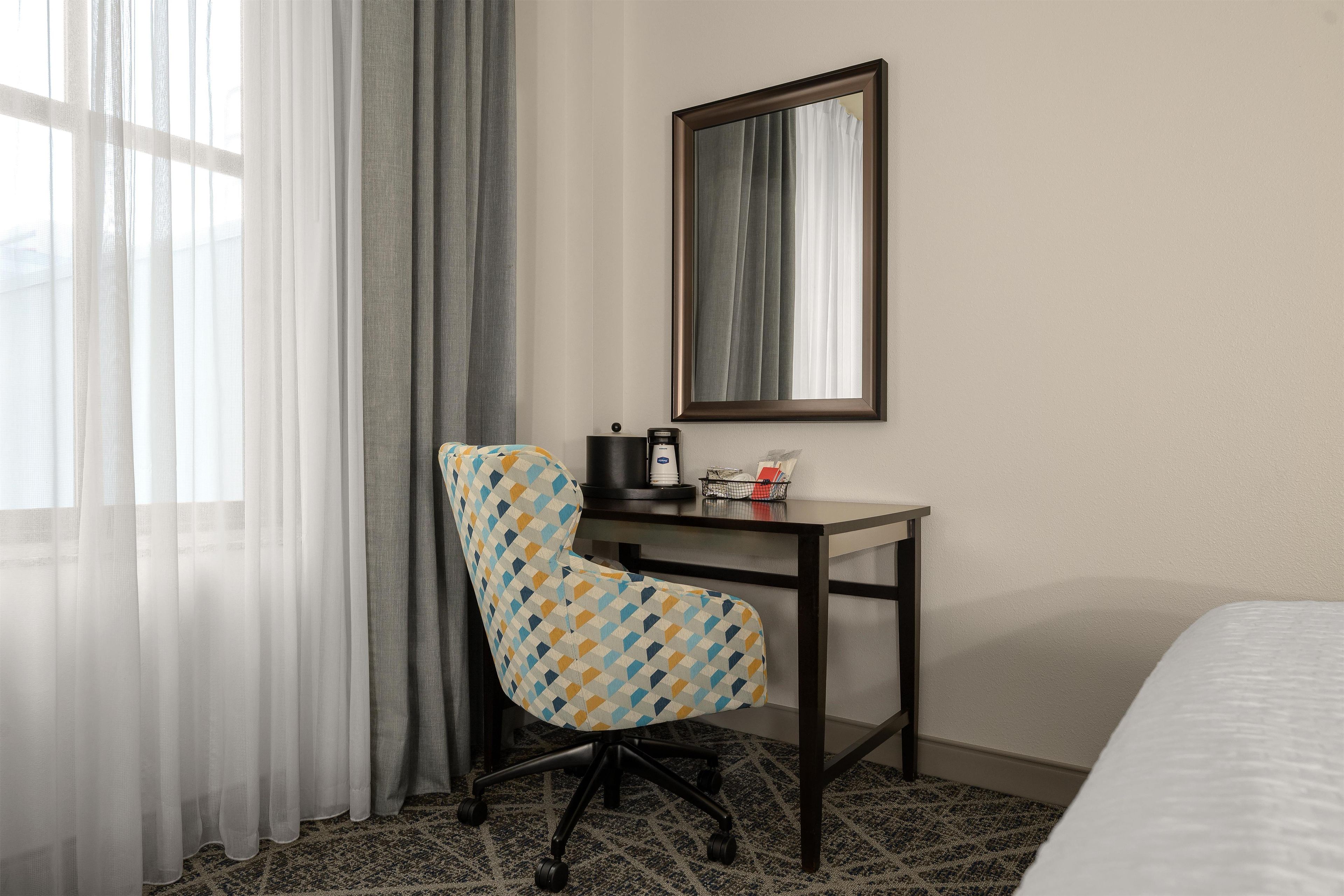 Una camera d'albergo con un letto, una scrivania con una sedia, una macchina per il caffè e uno specchio a parete.