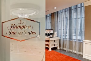 Uma área de recepção de hotel com uma placa que diz 'Hampton Inn & Suites'.