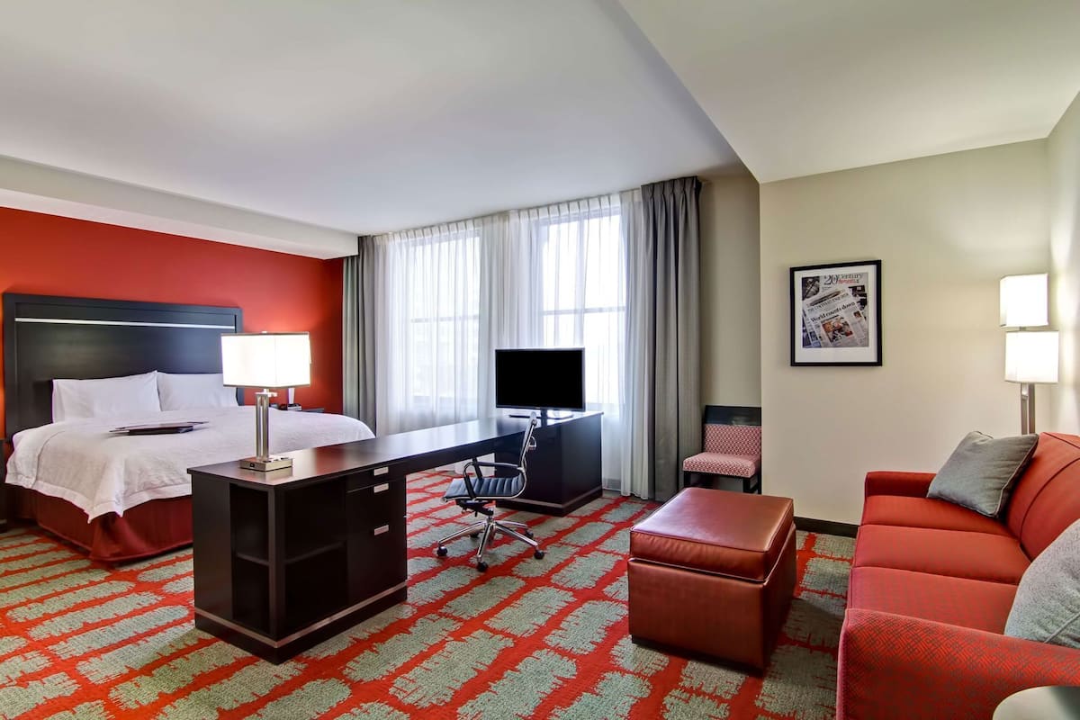 A hotel room with a bed, desk, TV, chair, couch, and a patterned carpet.