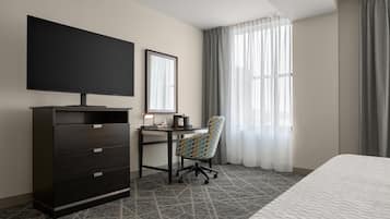 Habitación de hotel con cama, escritorio con silla, televisor, armario y ventana con cortinas.