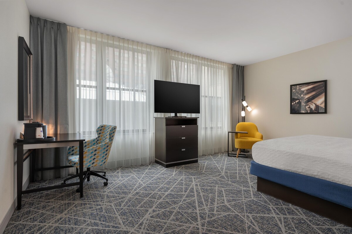 Una habitación de hotel con una cama, un escritorio con televisor, una silla y una lámpara.