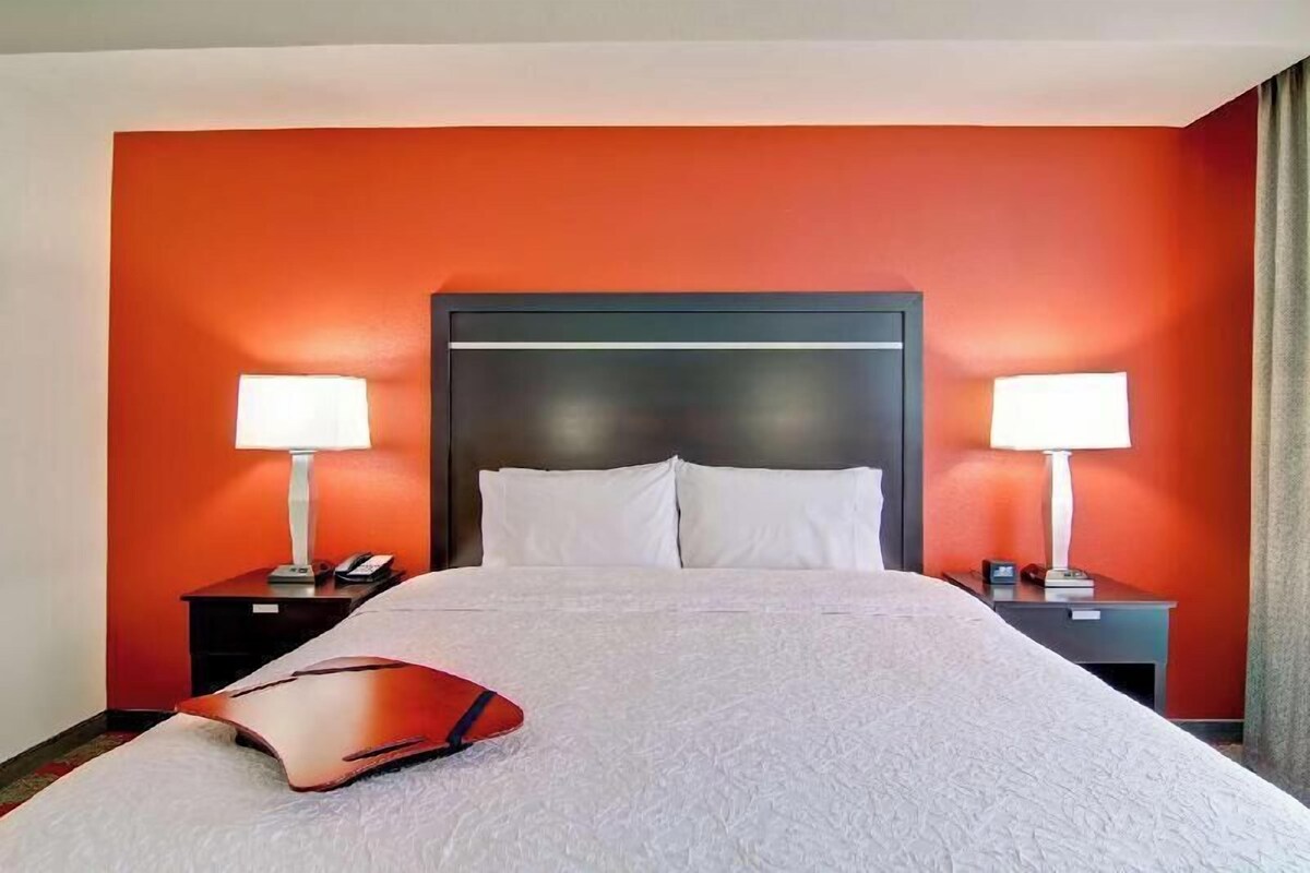 Una habitación de hotel con una cama grande, dos mesitas de noche con lámparas y una pared de acento roja.