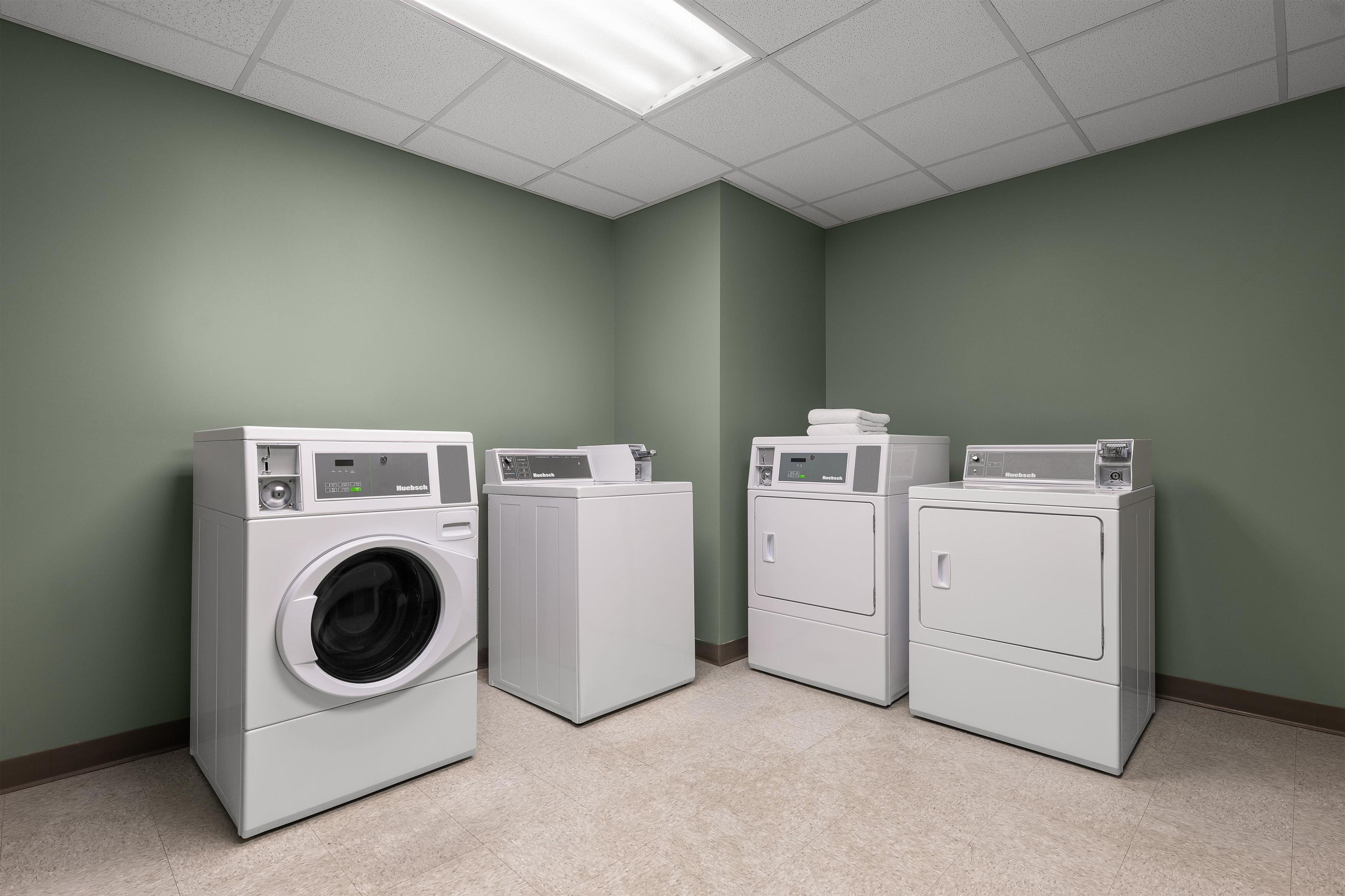 A laundry room with three white appliances, a green wall, and a tiled floor.
