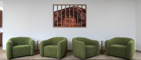 A room with three green armchairs, a white wall, and a framed picture.