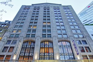 Un edificio alto de varios pisos con un estilo arquitectónico clásico, que presenta una entrada central con ventanales arqueados y un letrero destacado en la parte superior.