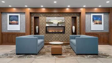 A modern lobby with two sofas facing a fireplace, a patterned wall, and framed pictures.