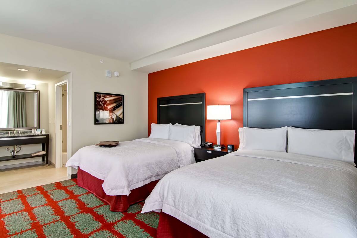 A hotel room with two beds, a desk, a mirror, and a red accent wall.