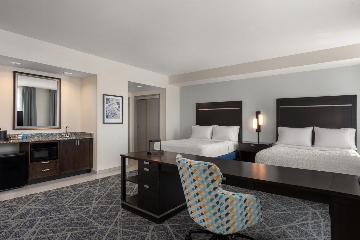 Habitación de hotel con cama, escritorio, silla y un espejo grande.