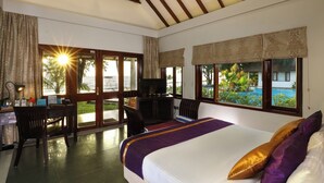 Habitación de hotel con cama, escritorio y sillas, ventanas amplias con cortinas y vista a una piscina.