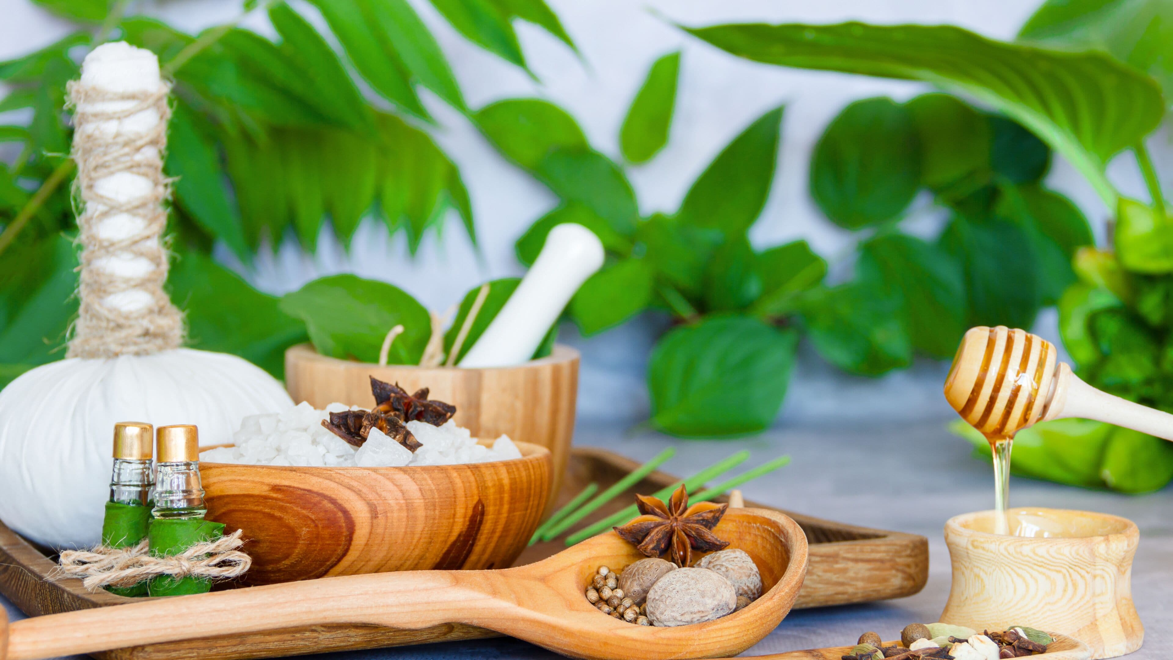 Una bandeja de madera con varios elementos naturales, como un objeto blanco, cucharas de madera y una cucharilla de miel.