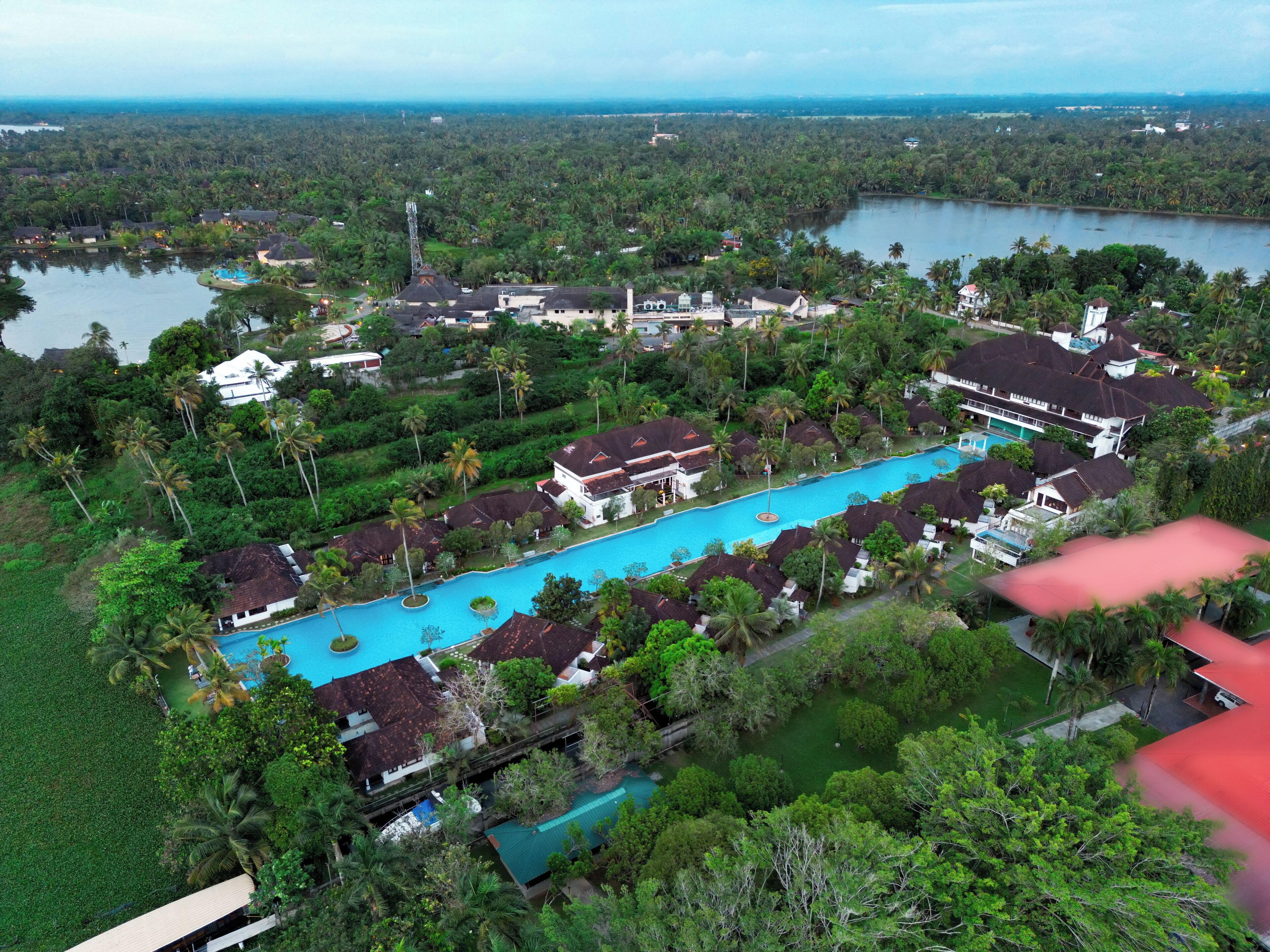 An aerial view of a resort with multiple swimming pools, lush greenery, and a lake in the background.
