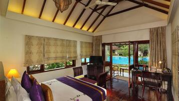 A bedroom with a bed, a desk, and a television. There is a window with curtains and a view of a pool.