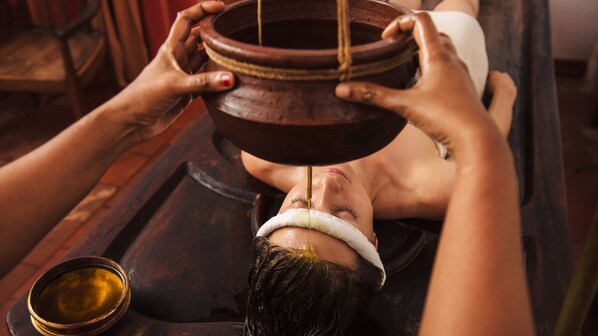 A person receiving a traditional treatment with a bowl and a liquid. - Rhythm Kumarakom (Kottayam)