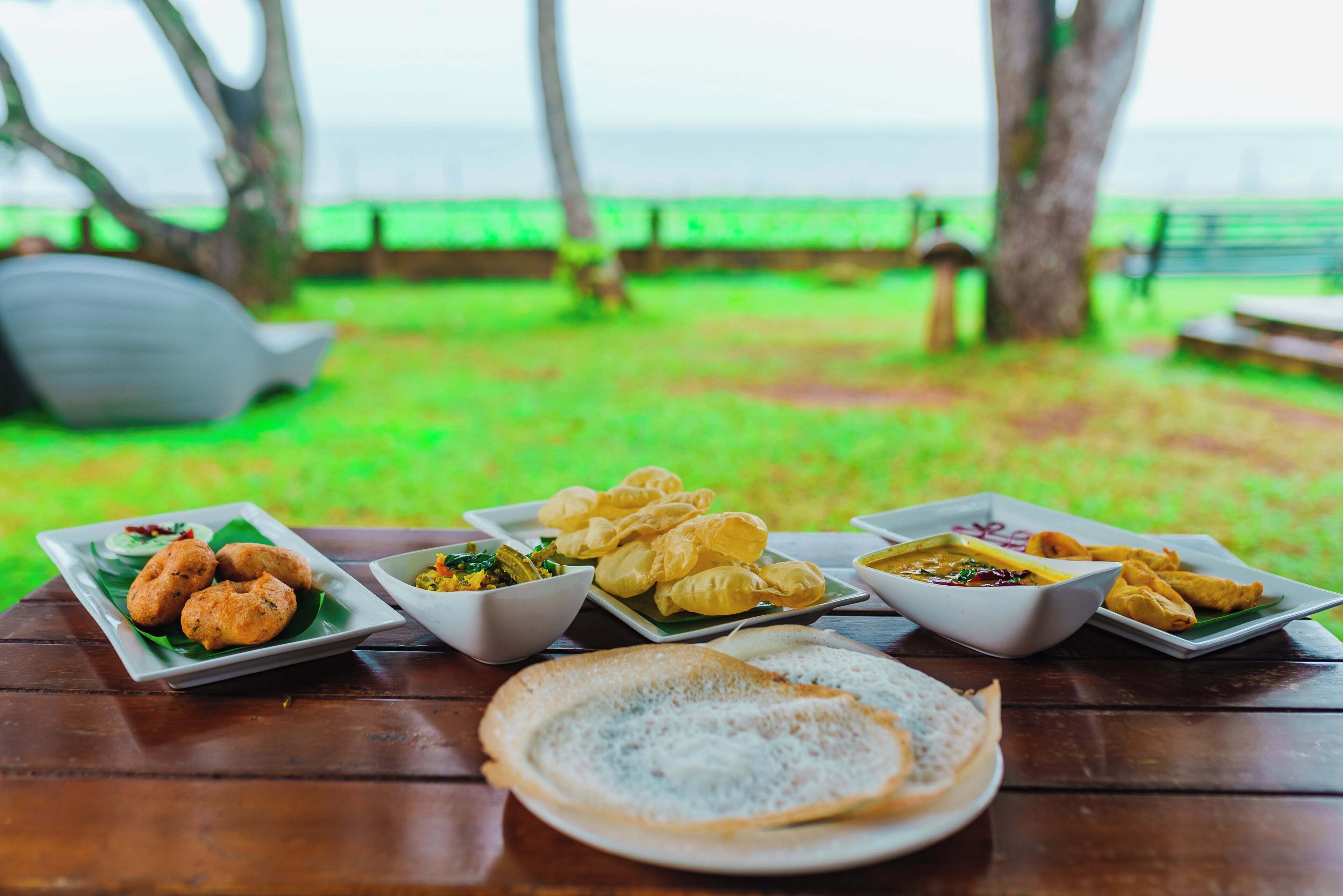 A table with various dishes and a plate of bread, set outdoors with a view of the sea.
