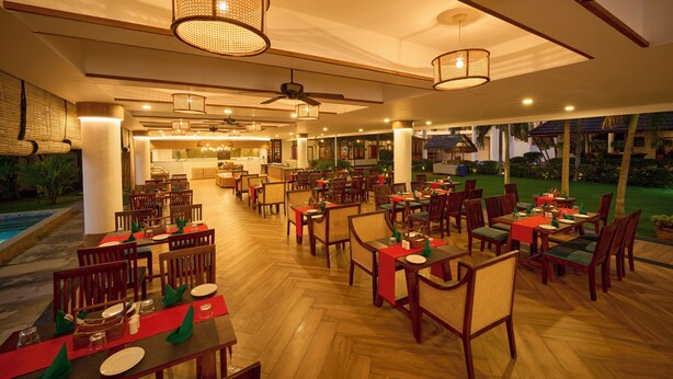 A spacious indoor dining area with multiple tables and chairs, ceiling fans, and ambient lighting. - Rhythm Kumarakom (Kottayam)