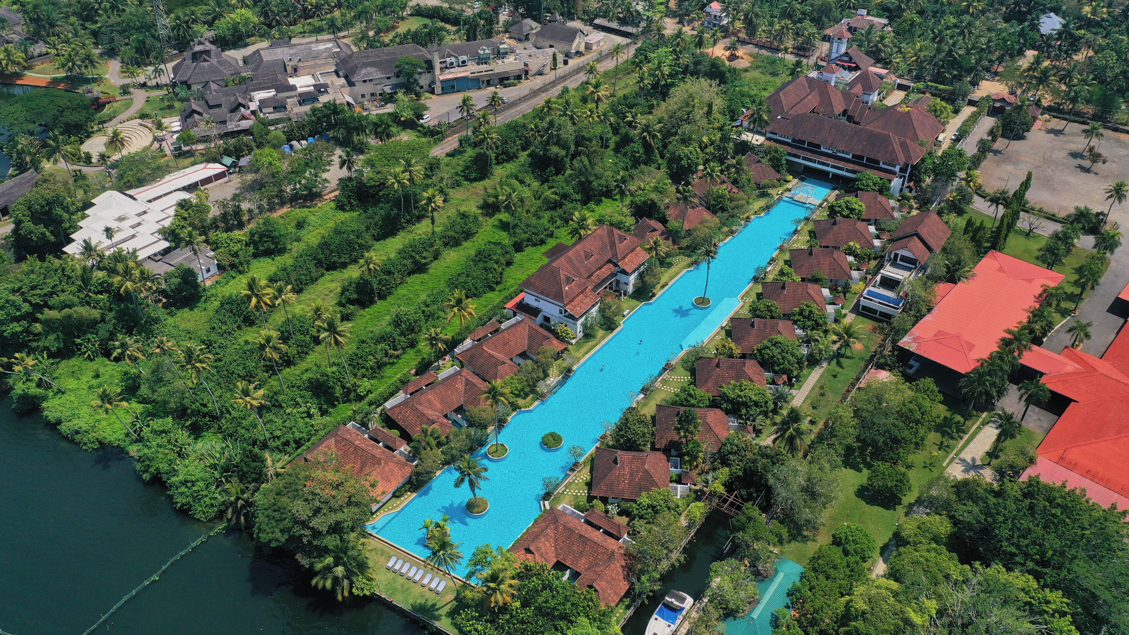 An aerial view of a resort with a long swimming pool, surrounded by lush greenery and tropical vegetation.