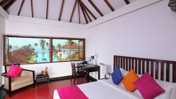A hotel room with a bed, a desk, a chair, and a window with a view of palm trees and buildings.