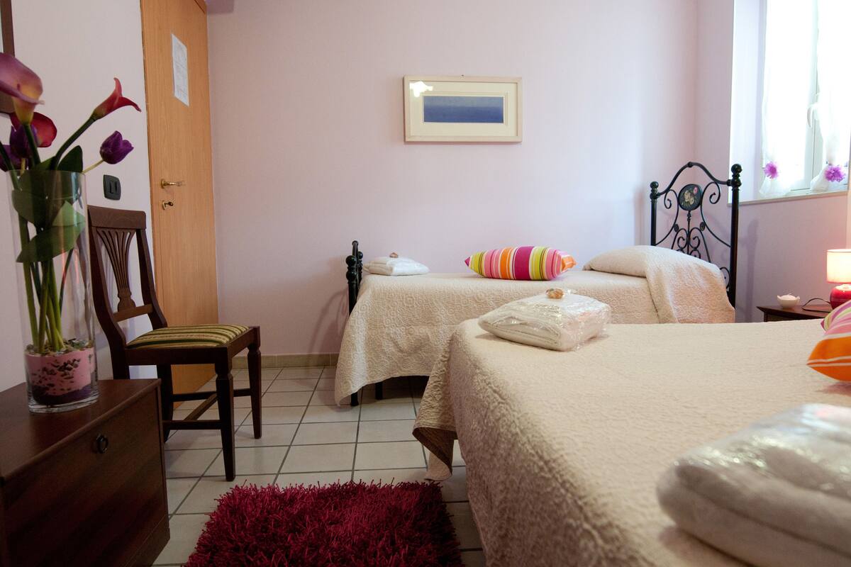 Un dormitorio con dos camas, una silla de madera, un tapete rojo y un jarrón con flores.