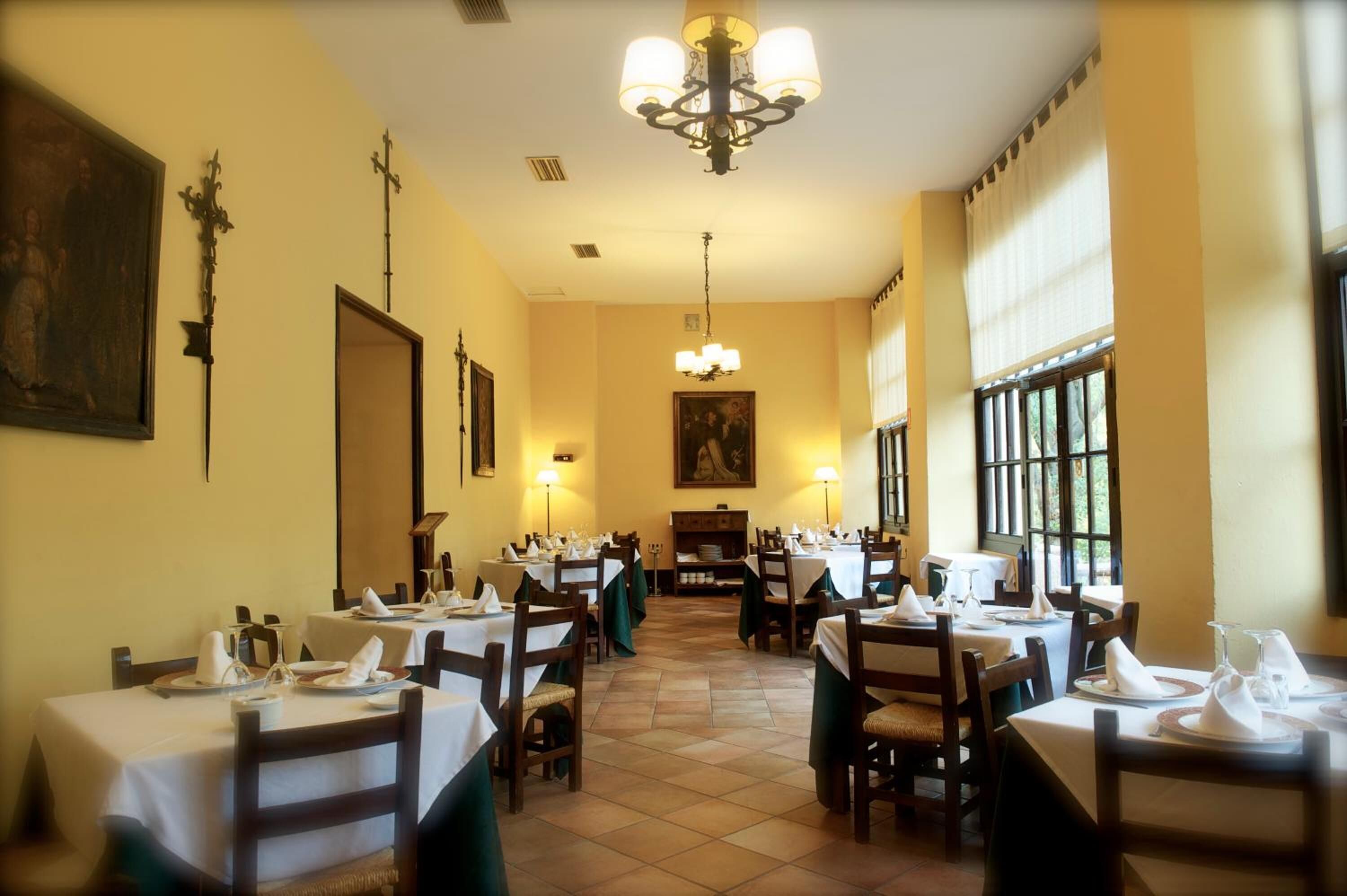 A restaurant with multiple tables set for dining, a chandelier, and paintings on the walls.