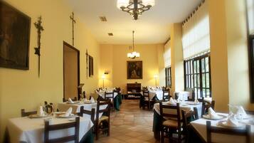 Un restaurante con varias mesas dispuestas para comer, una araña y pinturas en las paredes.