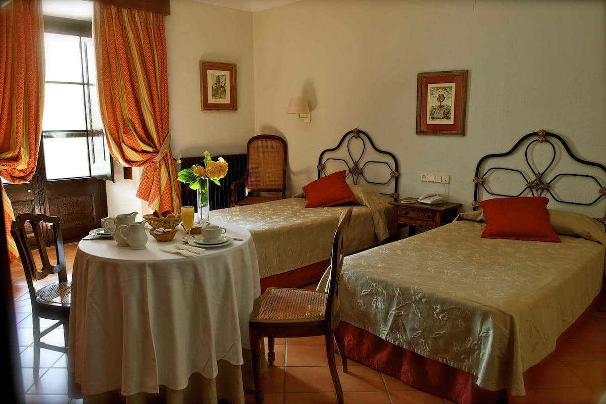 Habitación de hotel con dos camas, una mesa de comedor con alimentos para el desayuno, una silla y un jarrón con flores.