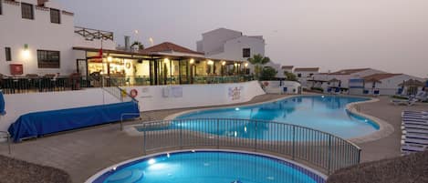 A swimming pool area with a dolphin mosaic, lounge chairs, and a bar/lounge area with outdoor seating.
