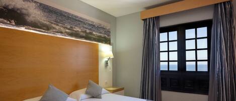 A hotel room with a large bed, a nightstand, a lamp, and a window with curtains.