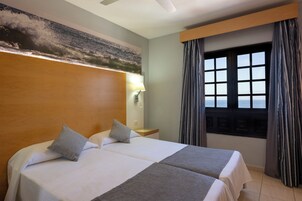 A hotel room with a large bed, a nightstand, a lamp, and a window with curtains.