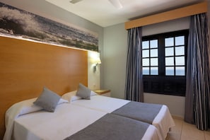 Una habitación de hotel con una cama grande, una mesita de noche, una lámpara y una ventana con cortinas.