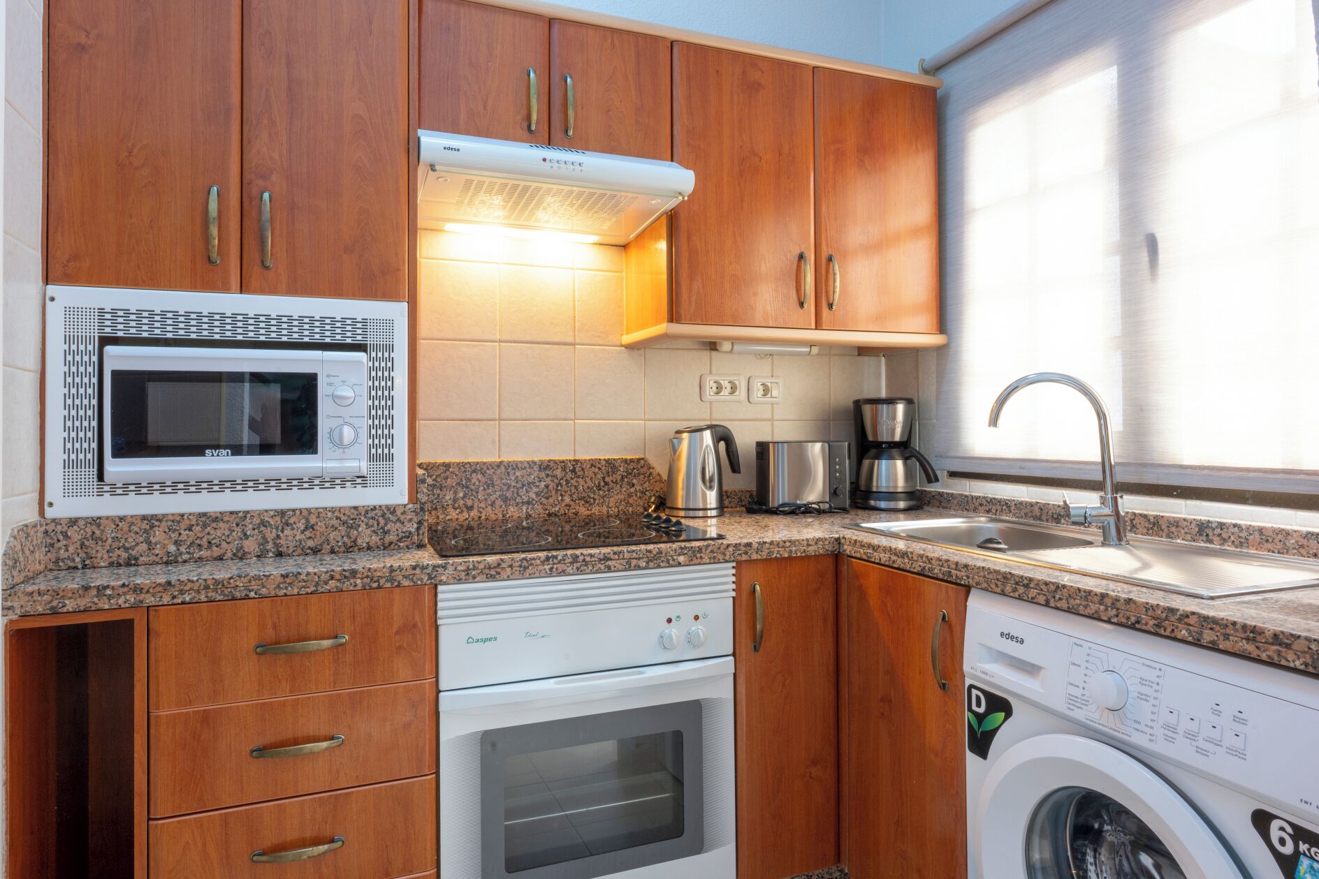 Una cocina compacta equipada con microondas, horno, cafetera y lavadora.