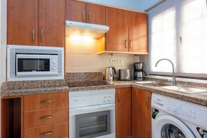 Una cocina compacta equipada con microondas, horno, cafetera y lavadora.