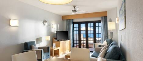 Habitación de hotel con balcón, televisor, mesa de comedor y asientos.