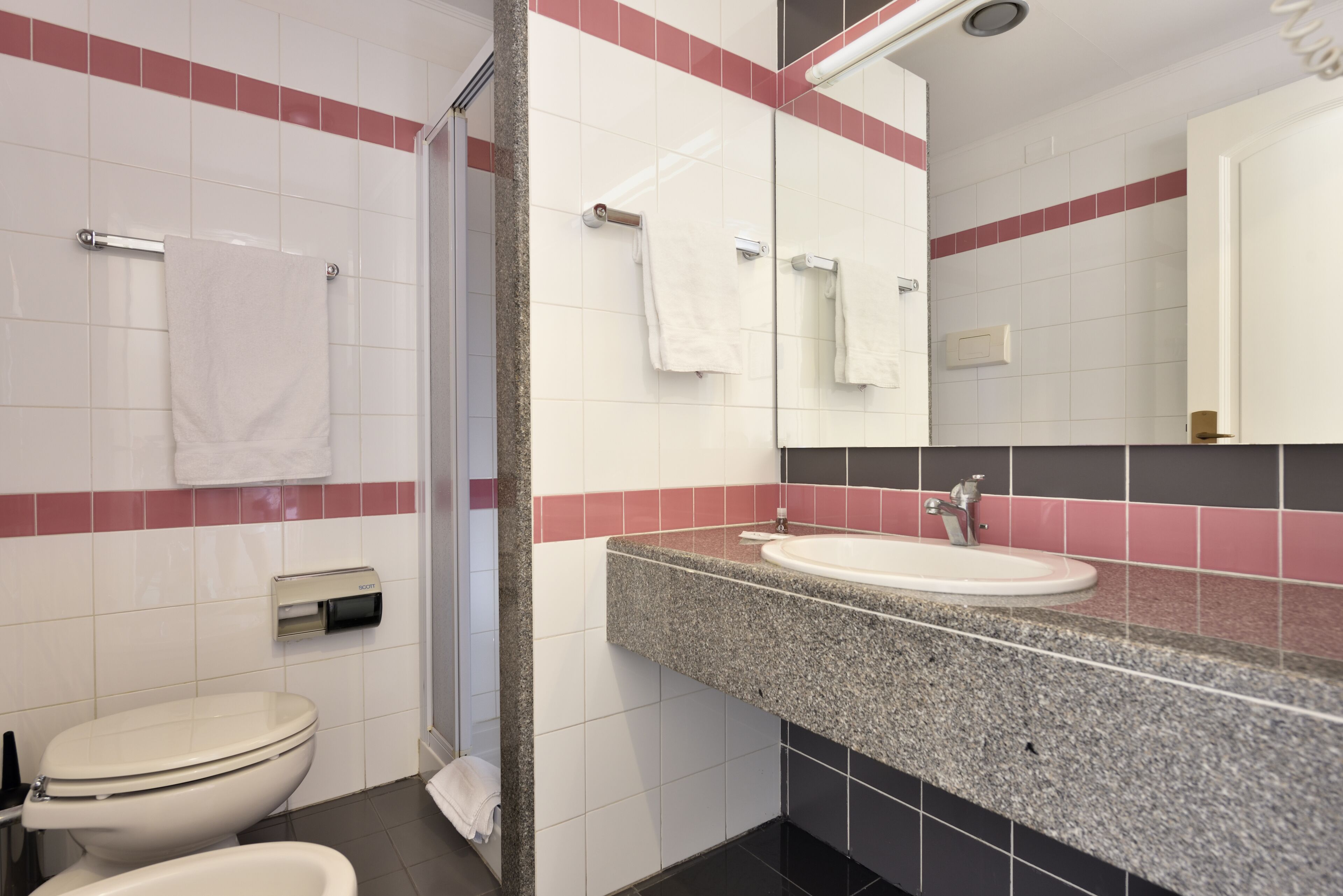 A modern bathroom with a white toilet, a sink with a granite countertop, and a mirror above the sink.