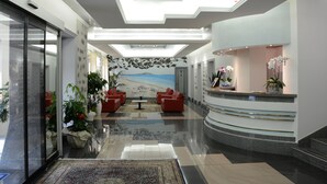 Un hall d’entrée moderne avec un comptoir d’accueil, des canapés rouges et une fresque représentant une scène de plage.