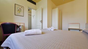 A hotel room with a bed, a chair, a desk, and a door.