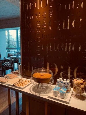 A breakfast buffet with a cake on a glass stand, various pastries, and condiments.