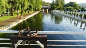 A canal with a bridge in the background, a railing in the foreground, and trees lining the path.