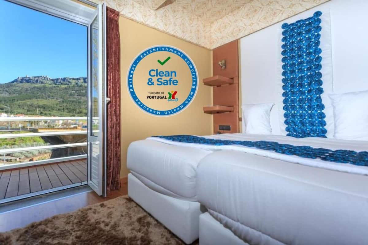 A hotel room with a bed, a large window, and a wall sign reading "Clean & Safe".