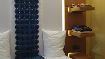 A hotel room with a bed, a decorative blue curtain, and a shelf with folded clothes.