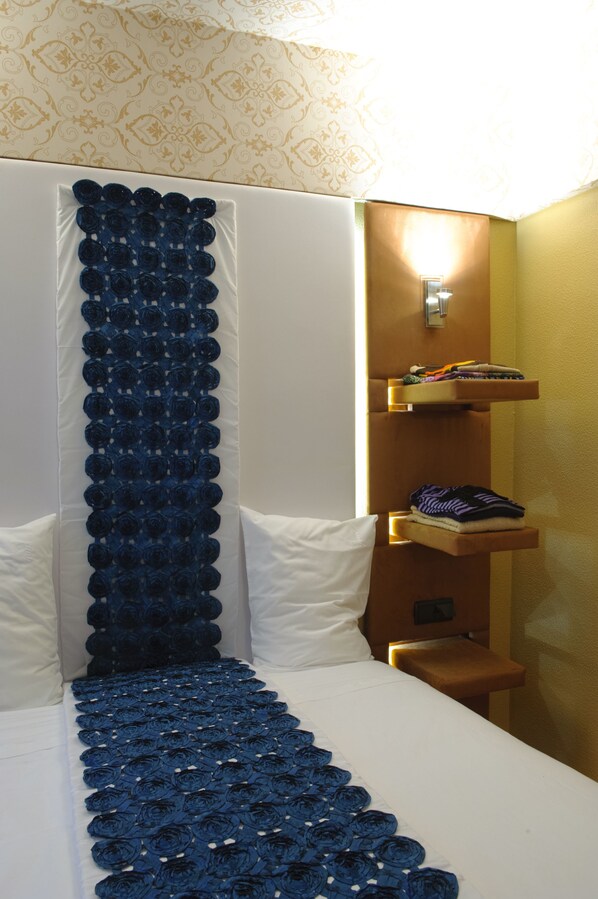A hotel room with a bed, a decorative blue curtain, and a shelf with folded clothes.