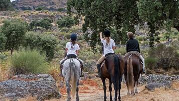 Tres personas cabalgando sobre un sendero de tierra con vegetación escasa y terreno rocoso al fondo.
