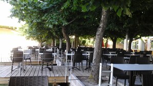 An outdoor seating area with tables and chairs, shaded by trees, overlooking a body of water. - Sever Rio Hotel (Marvao)