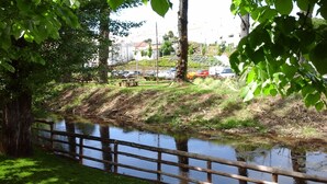 A riverside view with a wooden bridge, picnic tables, and parked cars in the background. - Sever Rio Hotel (Marvao)