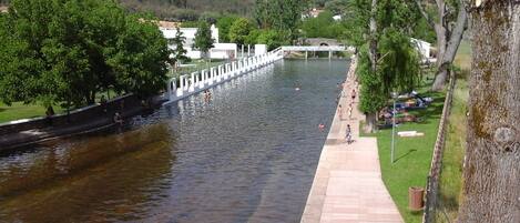 Un paseo fluvial con un puente, árboles y una zona cubierta de césped.