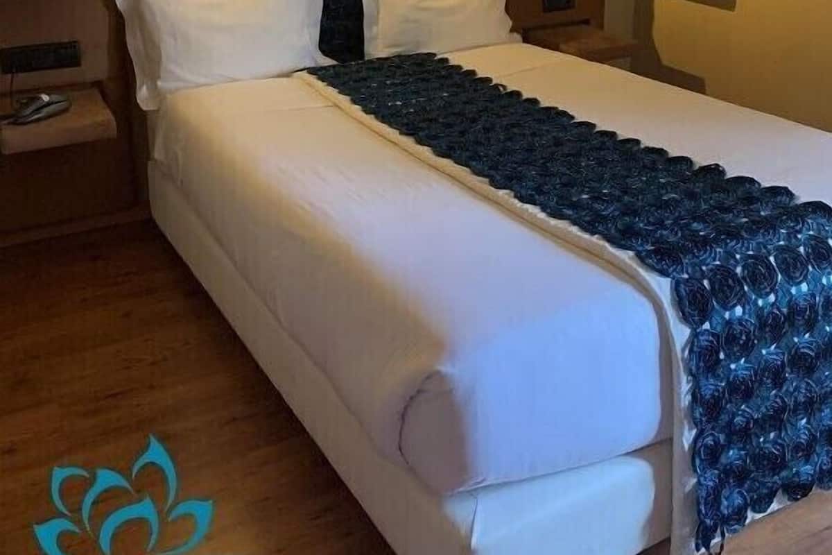 A modern hotel room with a large bed, a nightstand, and a wall-mounted shelf.